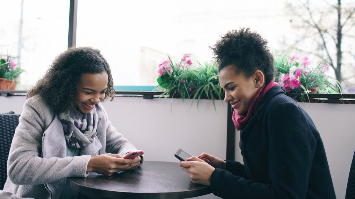 Two women laughing while looking at their phones.