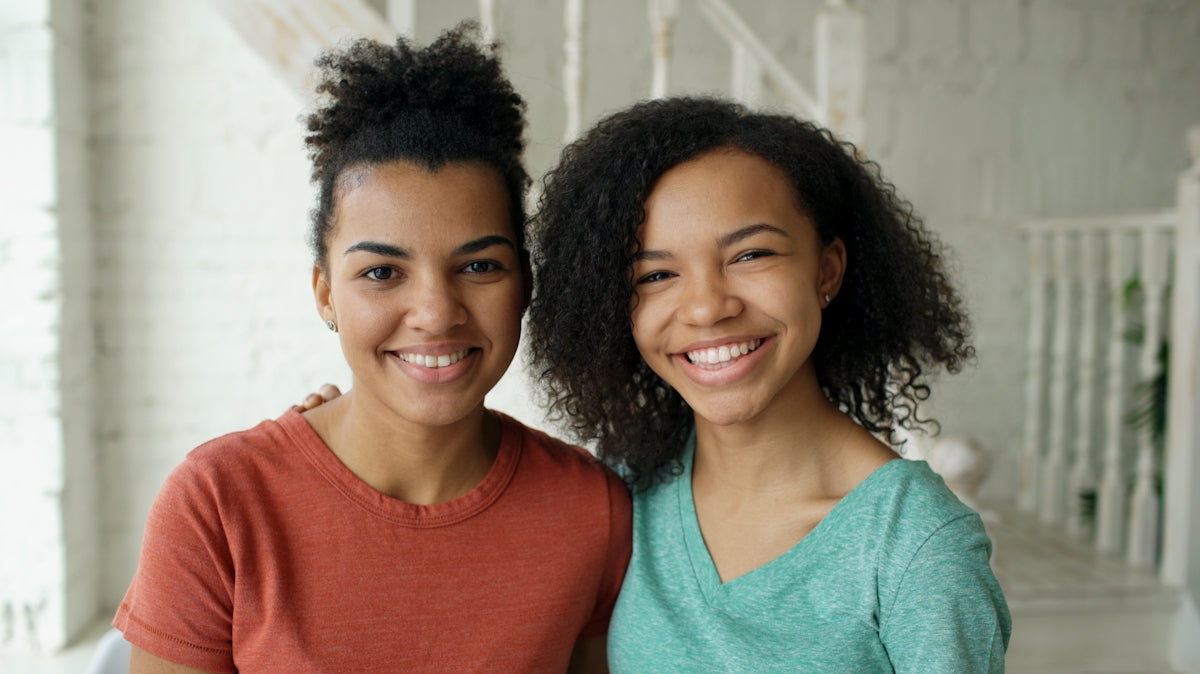 Two smiling young women standing together indoors.