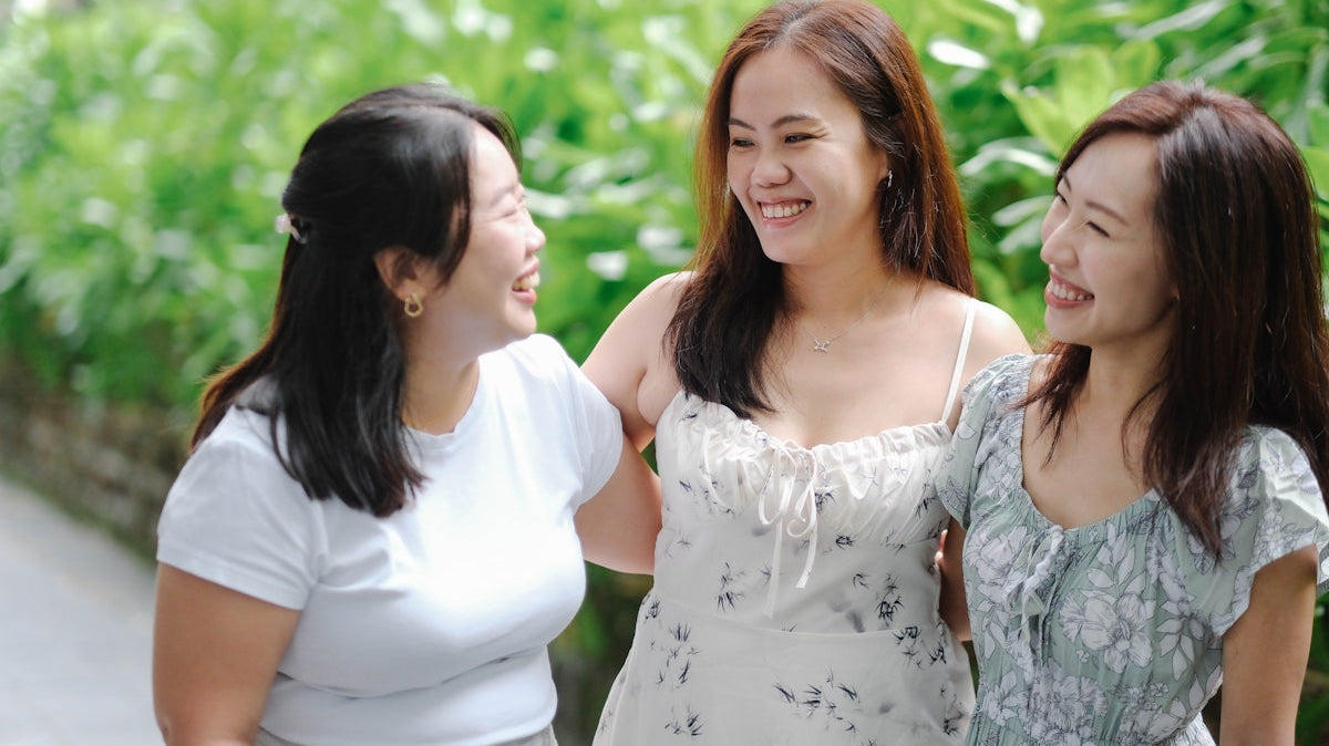 Three smiling women stand together outdoors.