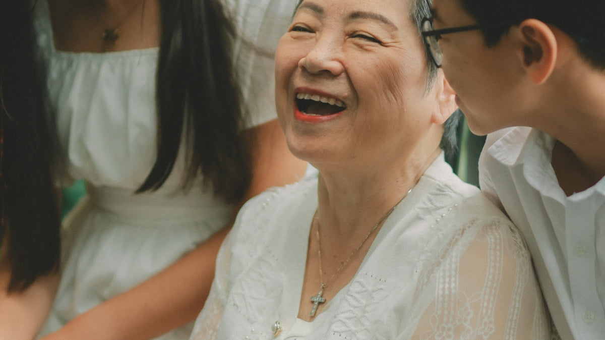 Grandmother laughing with her grandchildren, wearing white.