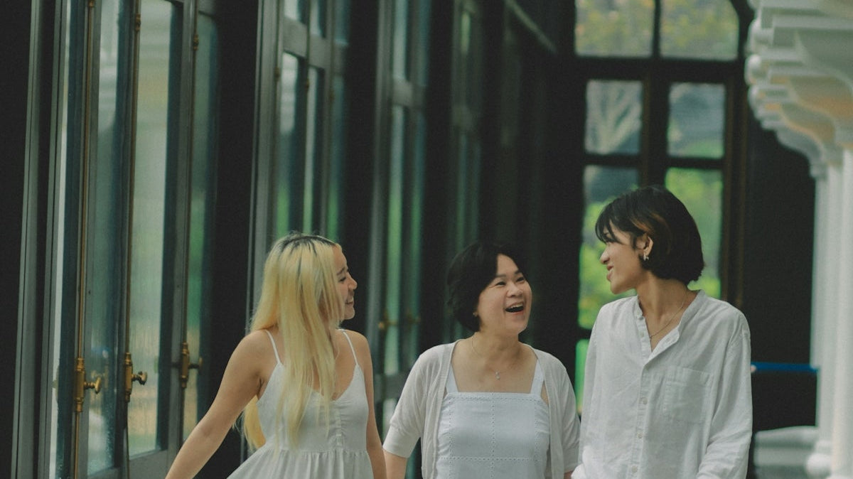 Three women in white walking together and smiling.
