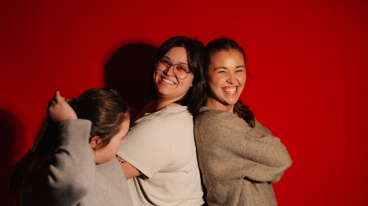 Three friends laughing against a red background
