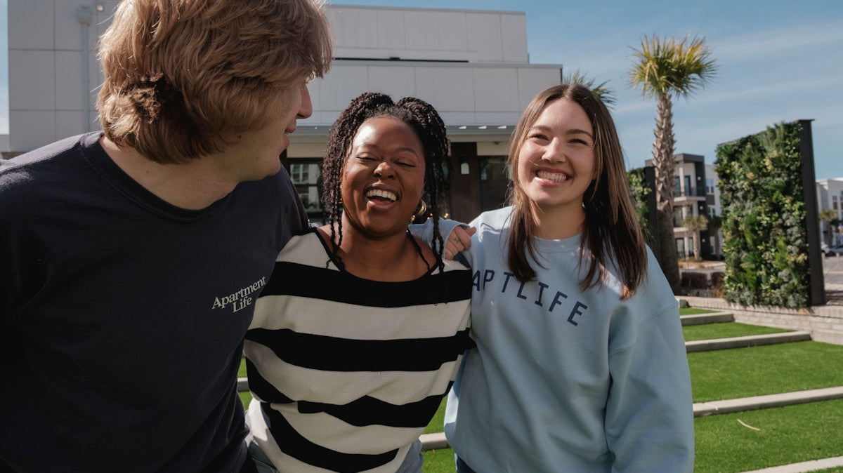Three smiling friends stand together outdoors.