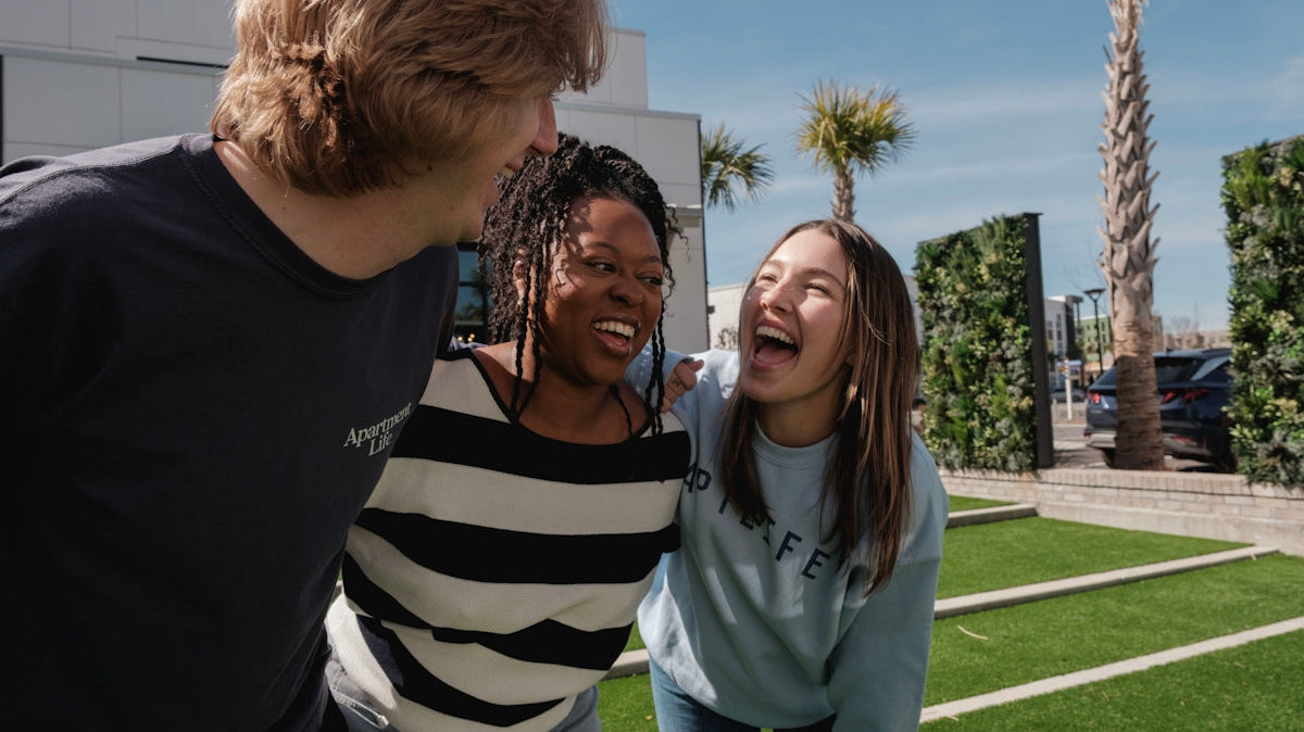 Three friends laughing together outdoors on a sunny day