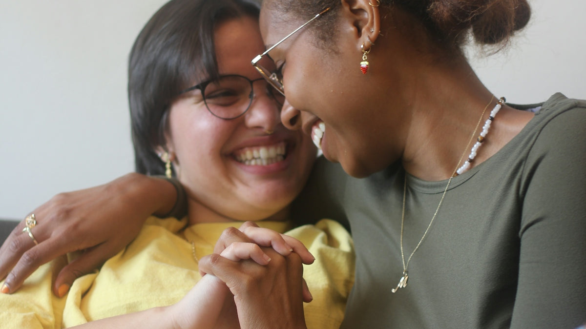 Two women laughing and holding hands on a couch