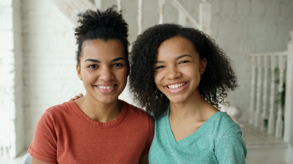 Two smiling young women standing together indoors.