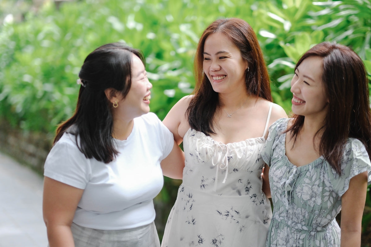 Three smiling women stand together outdoors.