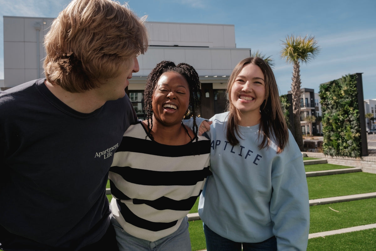 Three smiling friends stand together outdoors.