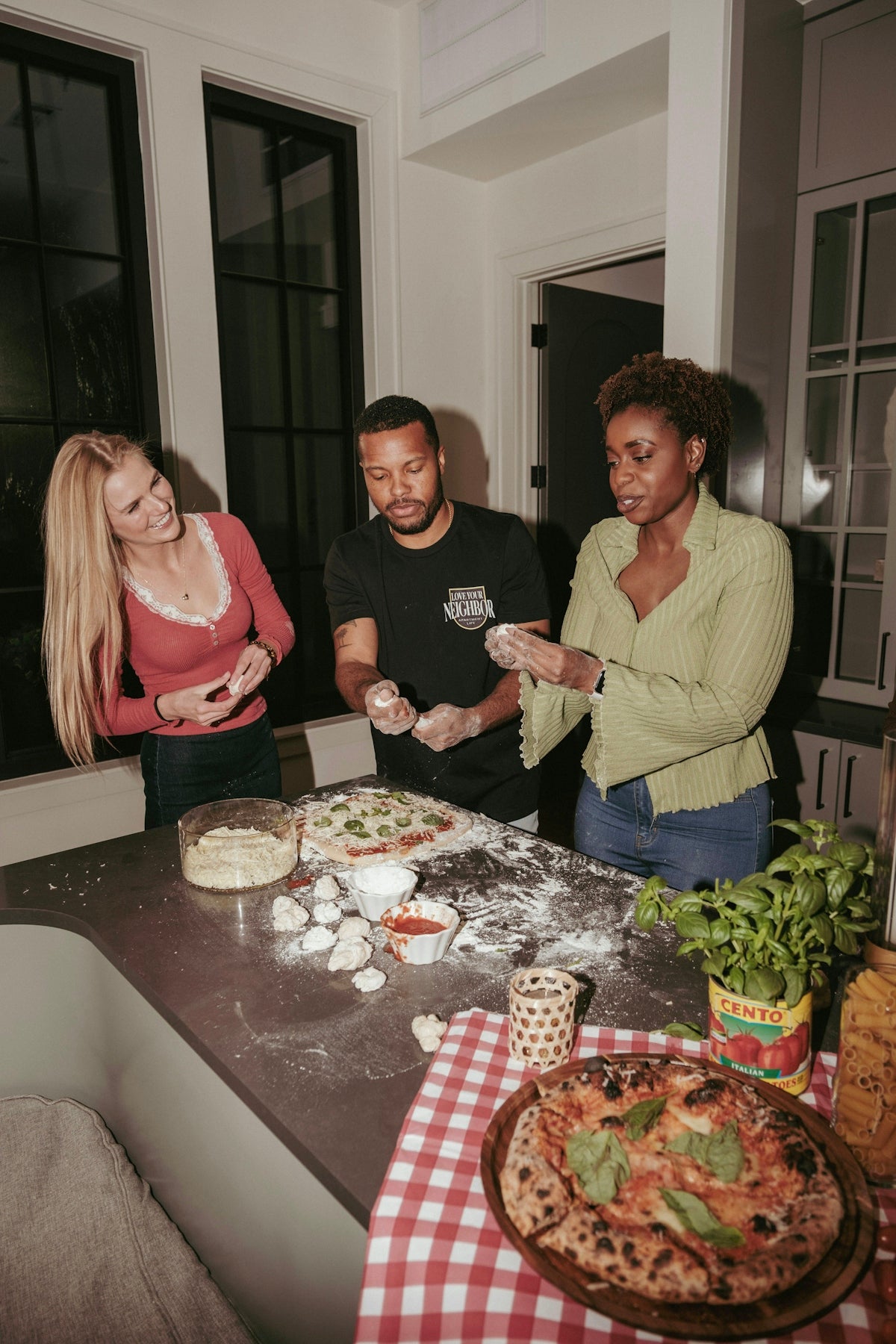 Three friends making pizza together in a kitchen.