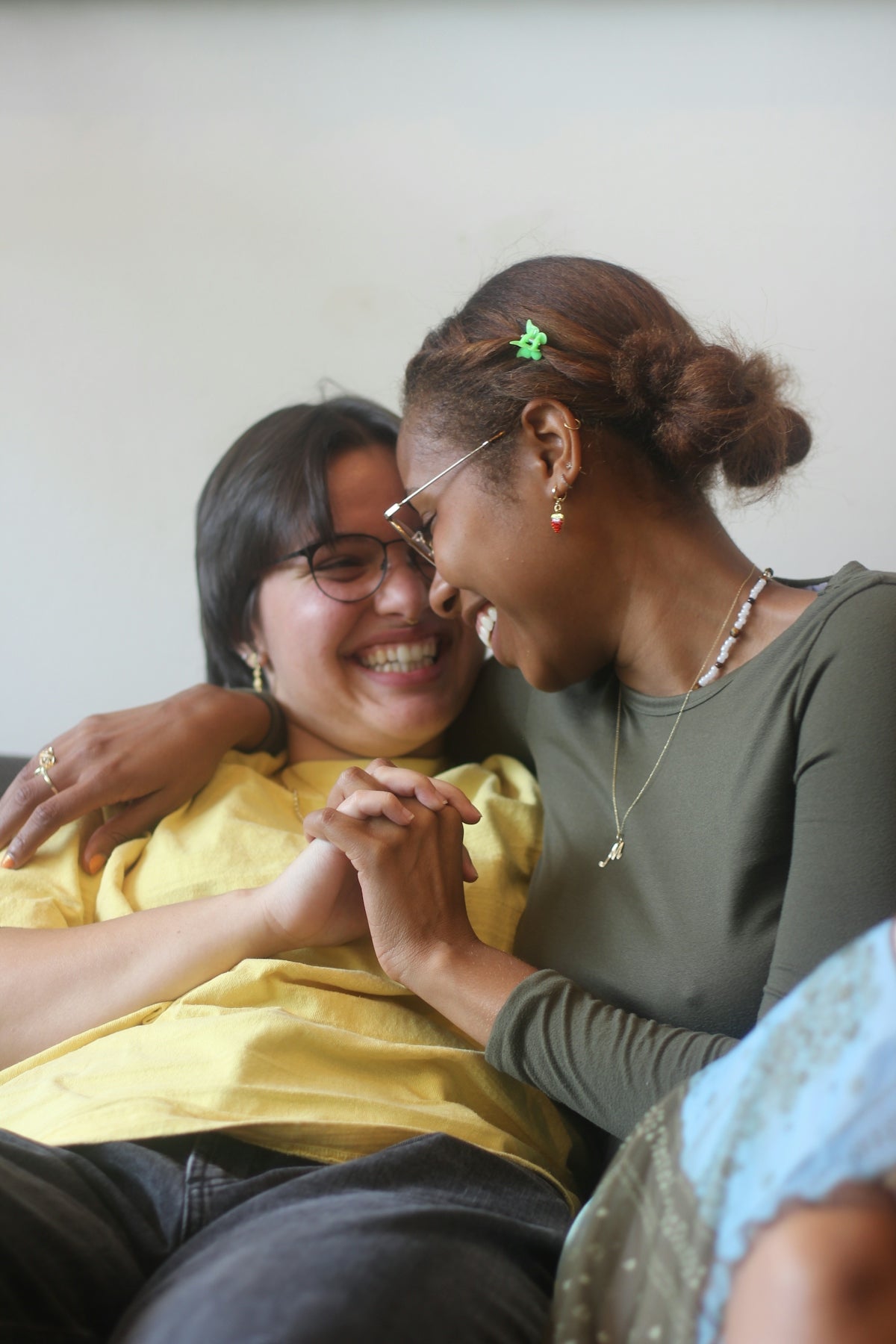 Two women laughing and holding hands on a couch